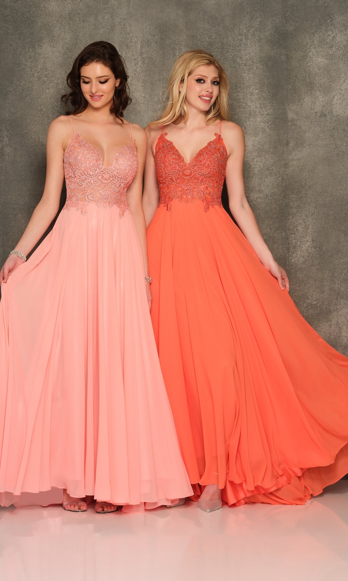 Two women stand side by side in Classic Long A-Line Prom Gown: Dave & Johnny A7248, featuring embroidered-lace bodices—one in light pink, the other in bright coral—set against a gray textured background.